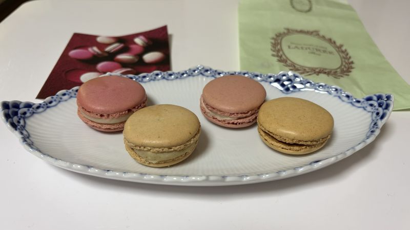 白い楕円皿に並んだピエール・エルメとラデュレのマカロン。背景にはラデュレの可愛い紙袋が見える。